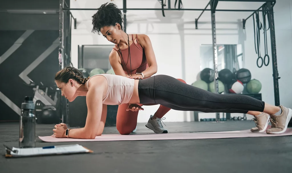 Female fitness trainer coaching a female client through a proper plank position.