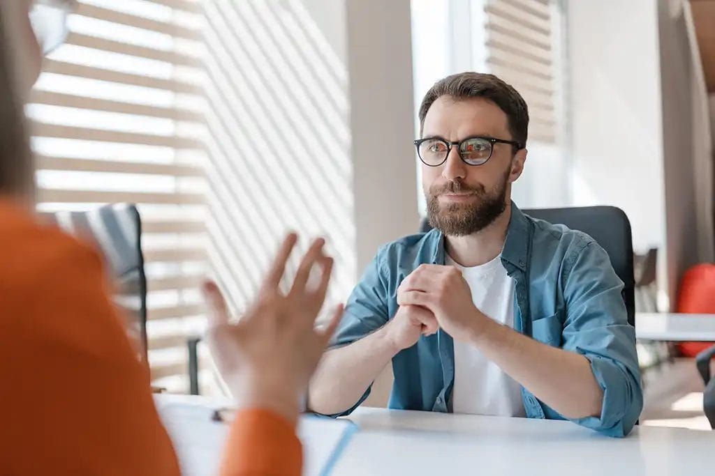 A man with glasses intently listening while he meets with a life coach.