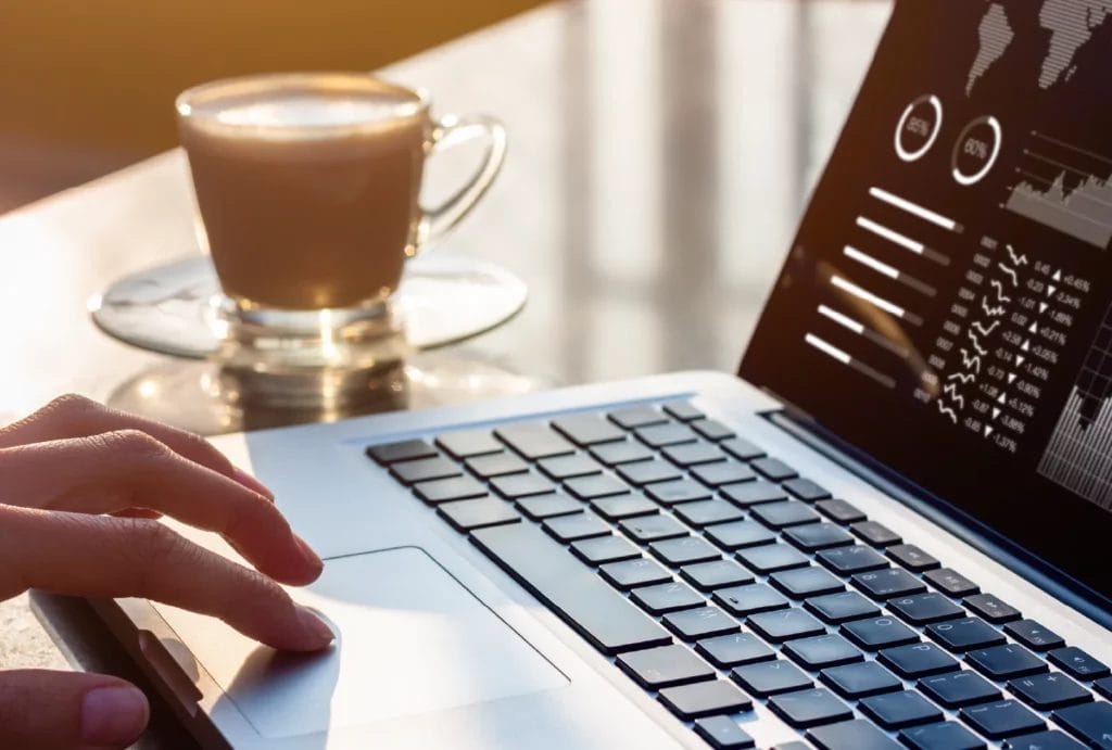 Close-up look of someone looking at stats on a laptop next to a cup of coffee
