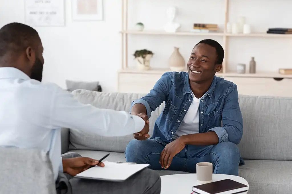 A young man meeting with another man over coffee. They are shaking hands and smiling at each other.