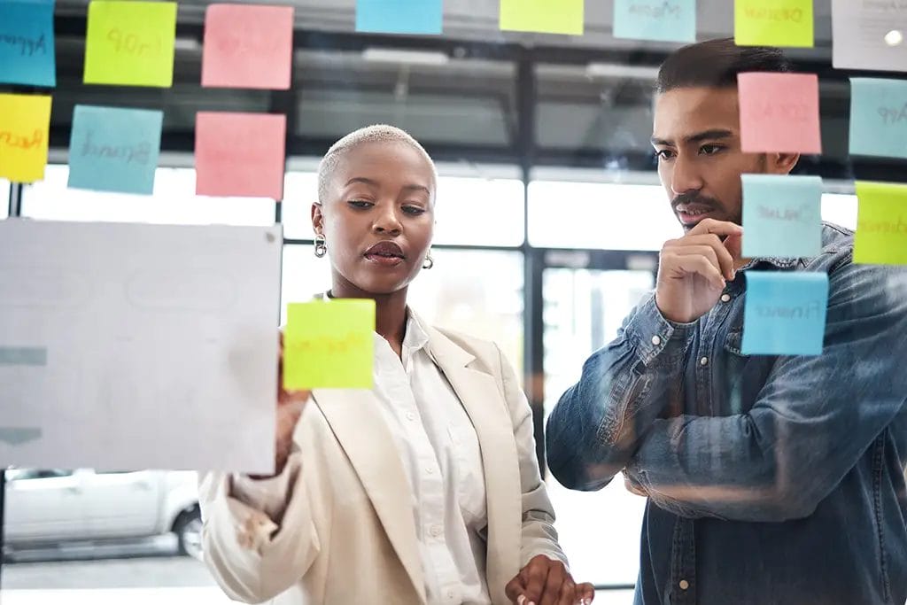 Two people looking at a window with multiple sticky notes.