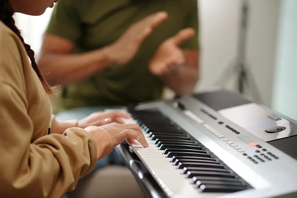 Home piano teacher claps to keep time as piano student plays on a keyboard.