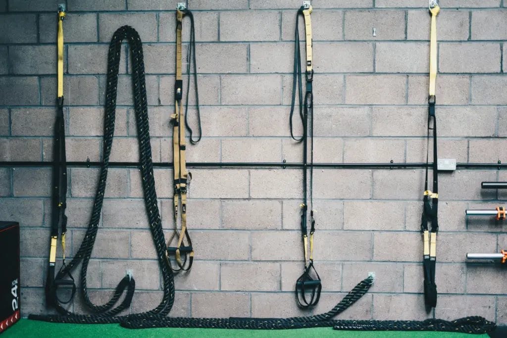 A series of TRX straps and a battle rope hanging on a cinder block wall.