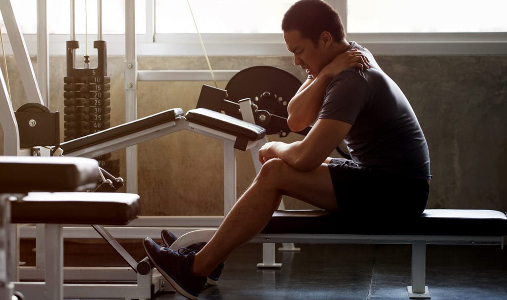 A man grips his shoulder while sitting on an exercise machine in the gym where he injured himself.