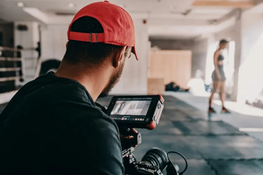 Man recording a personal trainer giving exercise instructions in a gym with recording equipment.