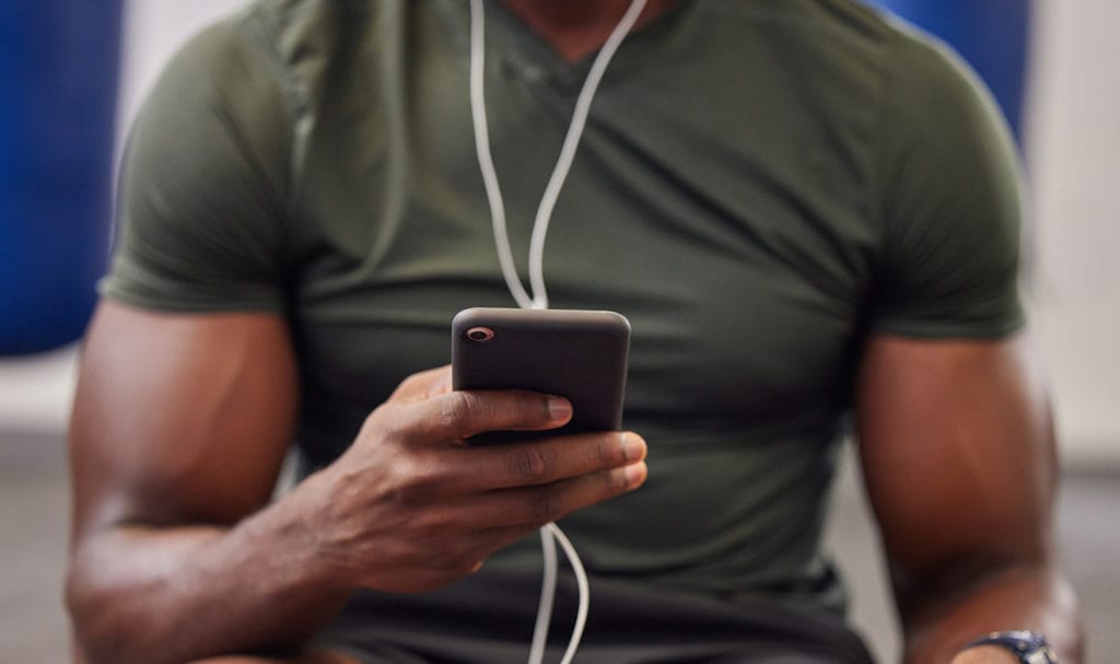 A closeup shot of a trainer using a smartphone with wired headphones.