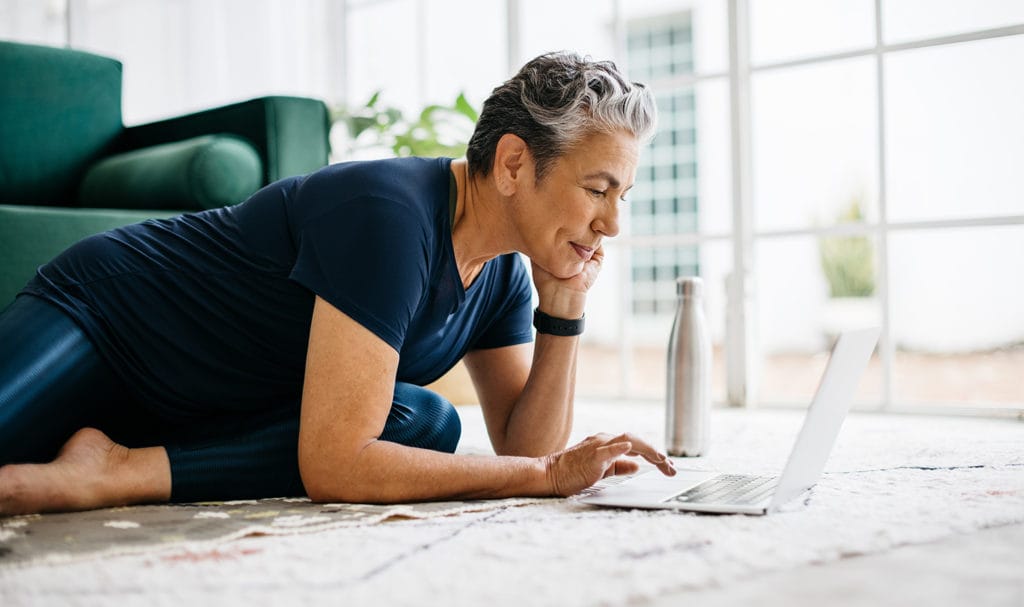 A yoga teacher works on her laptop on the floor of her home.