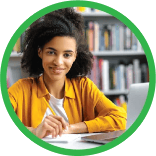 A tutor smiling at the camera and holding a pencil while working next to a laptop on a desk.