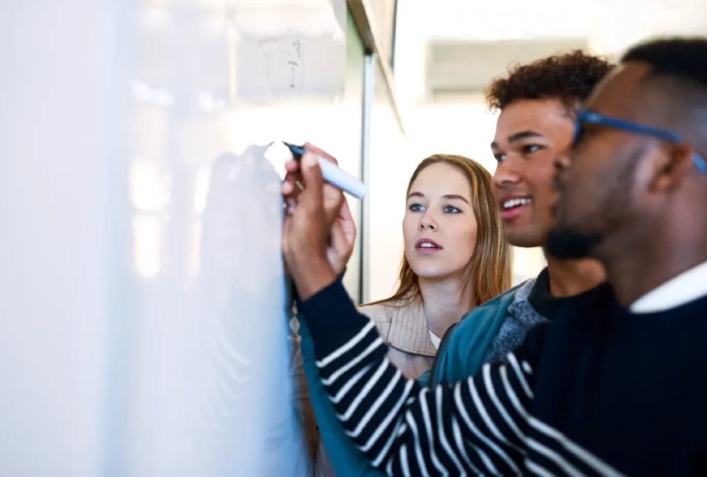 Tutor writing on a whiteboard for two engaged students.