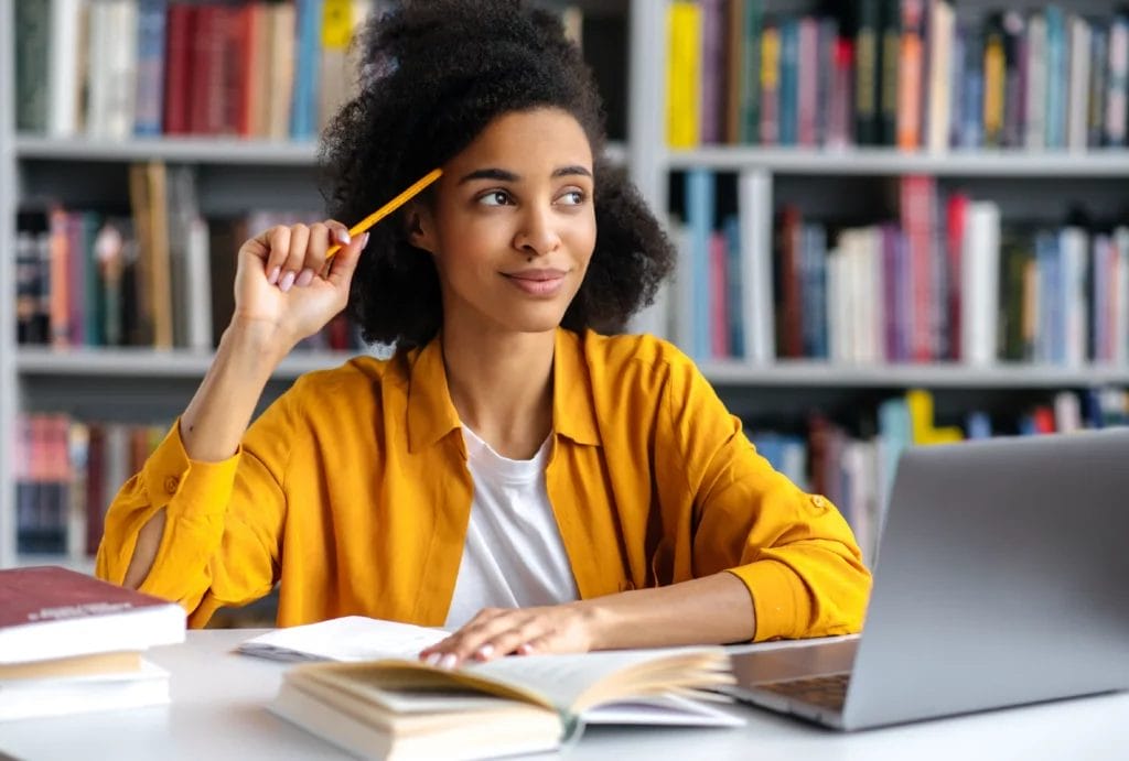 Smiling tutor in a library taps her temple with a pencil