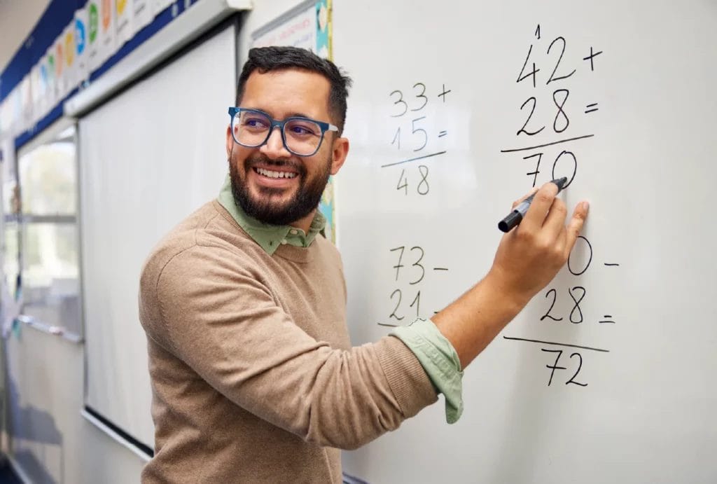 Smiling math educator solving equations on a white board.