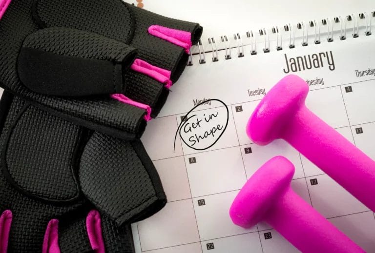 Black and pink fitness gloves and pink dumbbells set atop a spiral calendar opened to January with the first day circled with the words "Get in shape" written in.