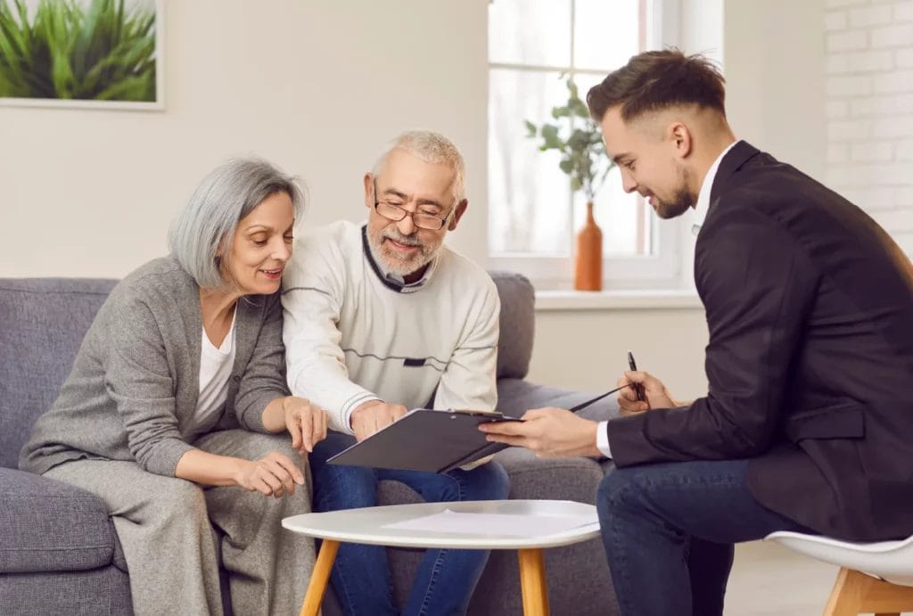 A retirement coach sits in front of an elderly couple in a coach at home.