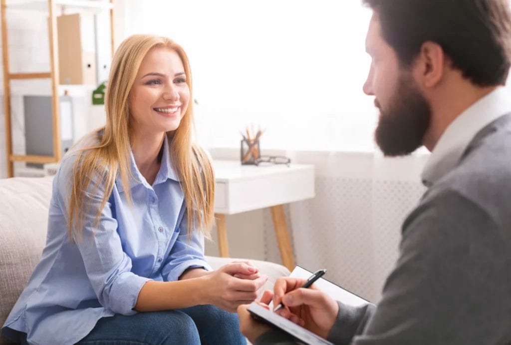 A woman smiles during a session with her life coach, who is taking notes in a journal.