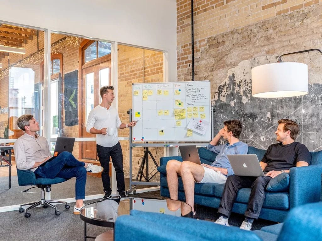 Group of people in a casual setting discussing notes on a whiteboard.