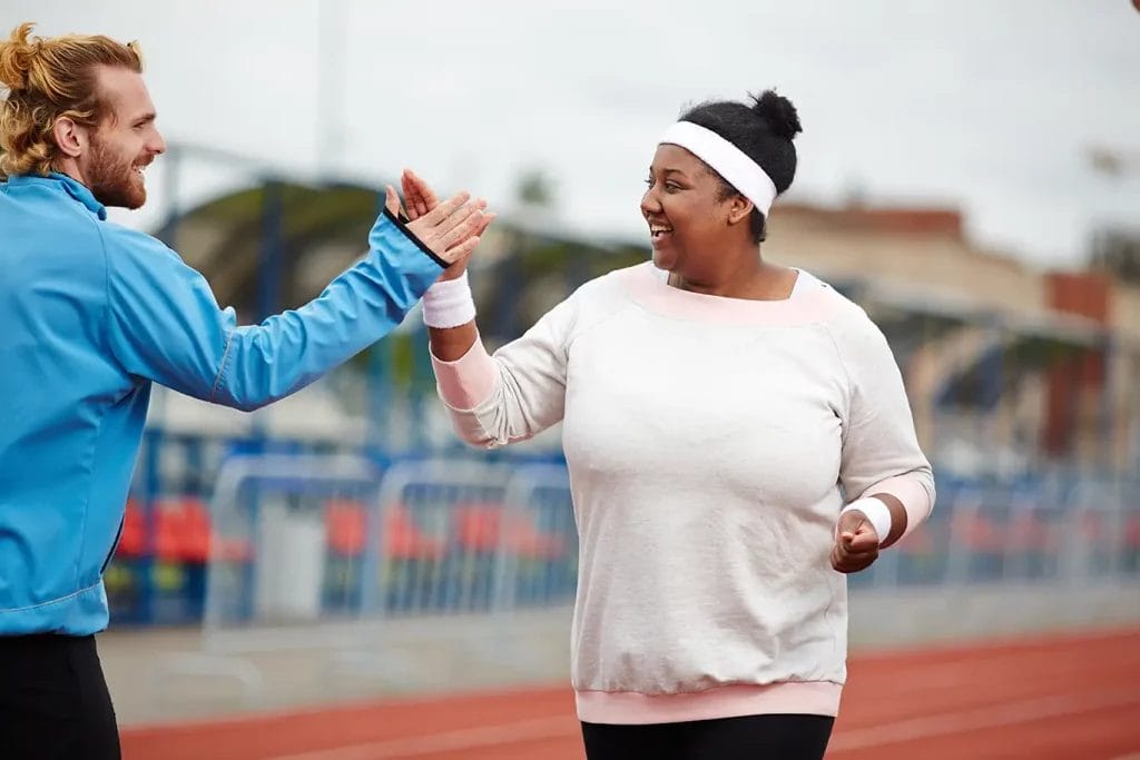A male life coach giving his client a high five while she works out, both smiling at each other.