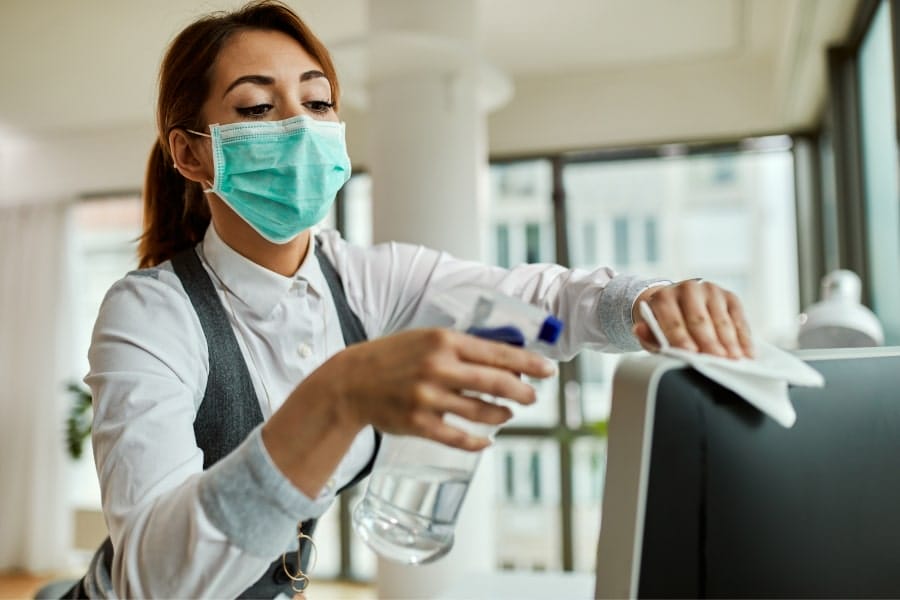 woman with mask on wiping down computer