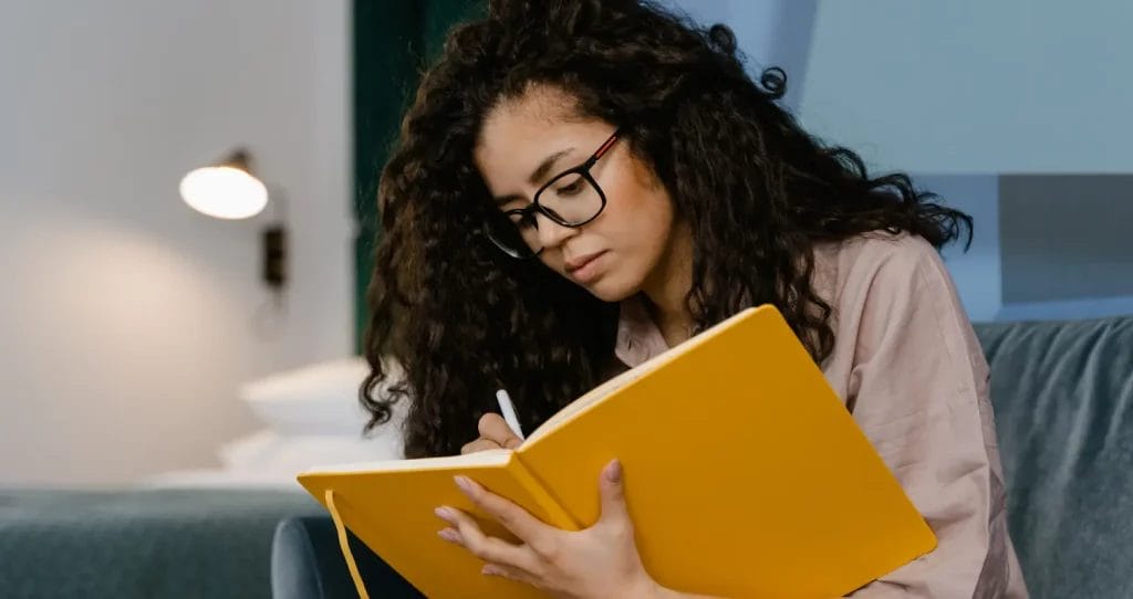 A woman holding a notebook writing intently inside.