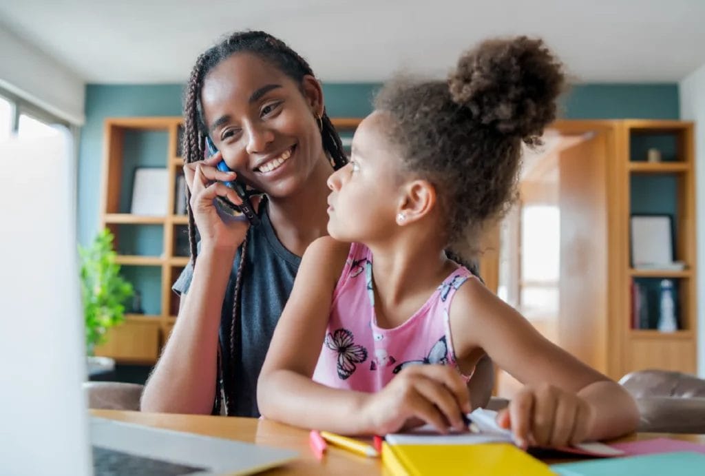 Mother talking on the phone while helping her daughter with homework