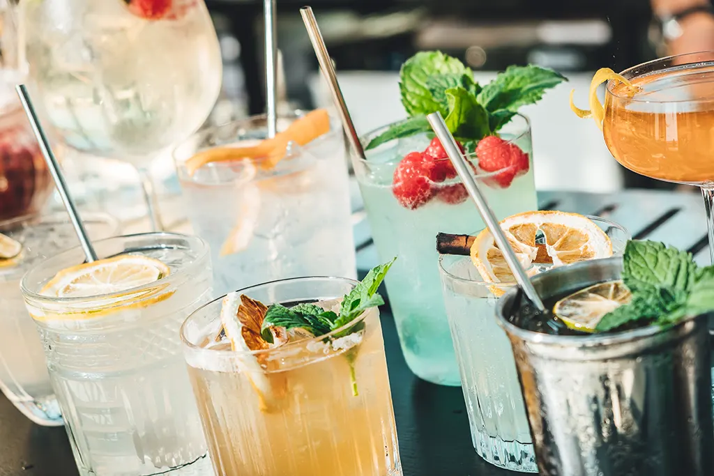 A close-up shot of several different types of cocktails on top of a bar, each with citrus and herb garnishes.