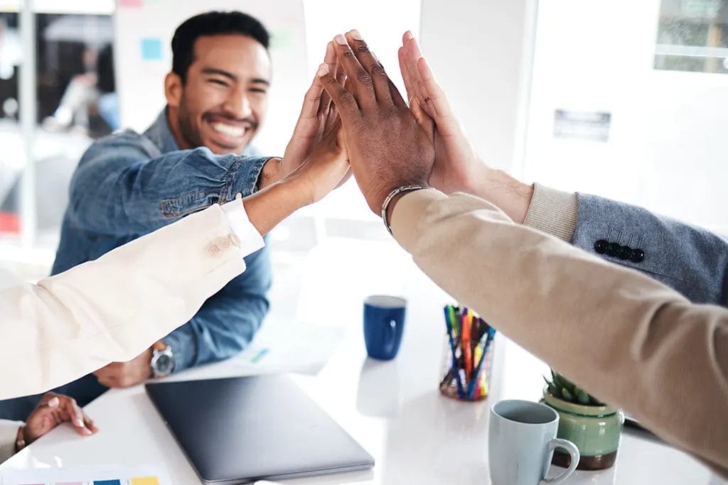 Four people around a table with there hands together in the air, high fiving each other.