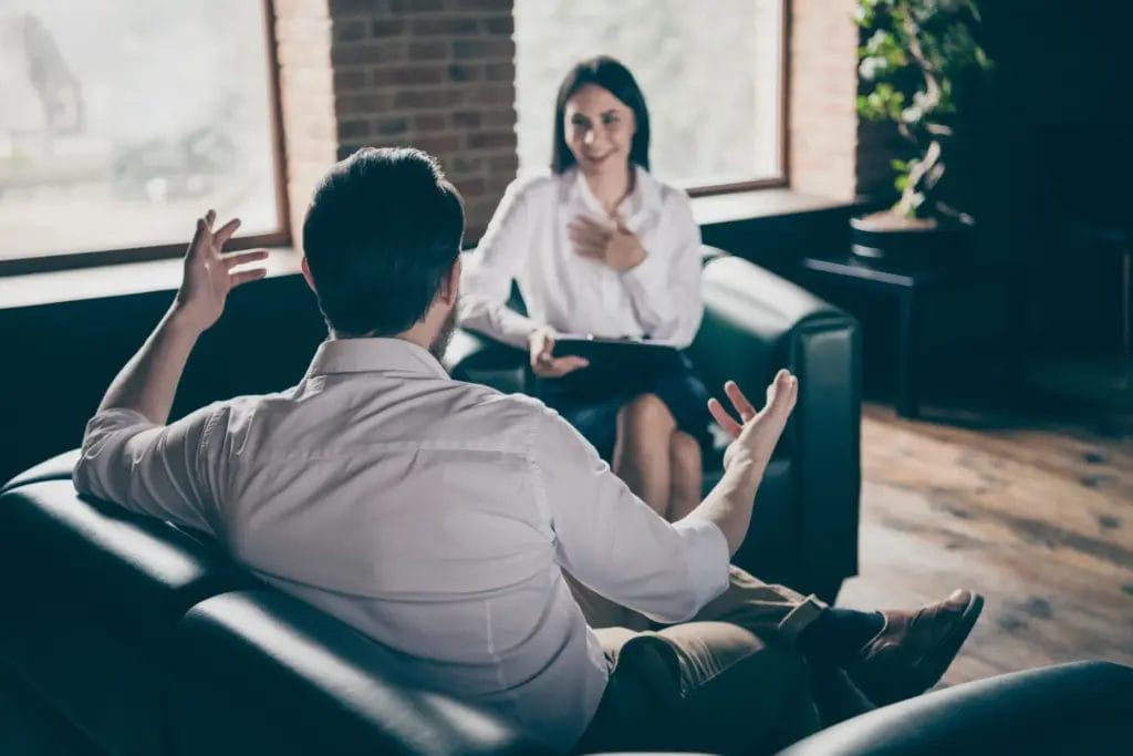 A life coach sits across from her client in a naturally lit office with hardwood floors and brick walls.