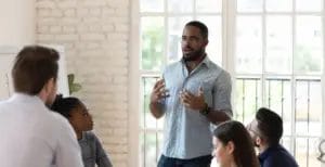 A male life coach stands in front of a group of professionals in a conference room