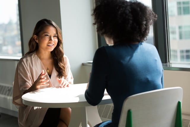 two women talk to one another at a table