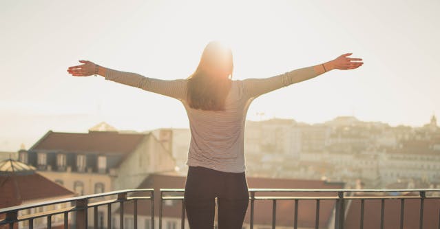 a woman stands with her arms outstretched joyously