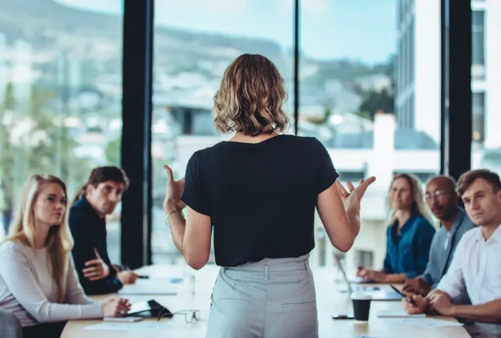 Speaker gestures while presenting to a group of businesspeople in a modern office