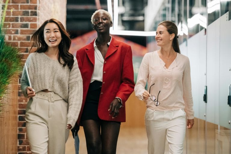 three professionally dressed women walk confidently down a hallway