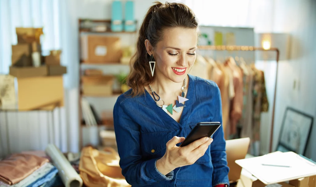 A woman smiles at her phone as she looks at her business liability policy online.