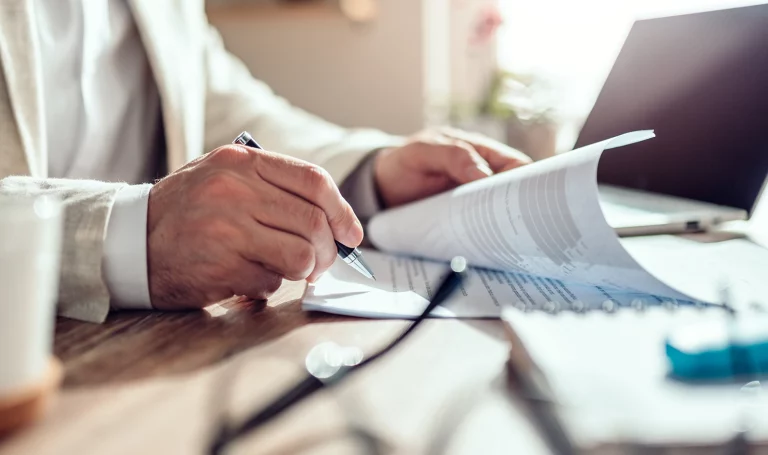 A close-up shot of a business owner looking through paperwork at a desk next to a laptop with a pen.