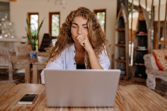 a woman sits thinking at a computer