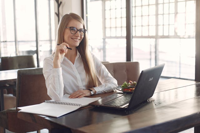 a smiling professional woman sits in front of an open computer