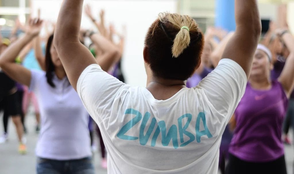 Zumba instructor in a white Zumba class shirt photographed from behind while teaching a class.