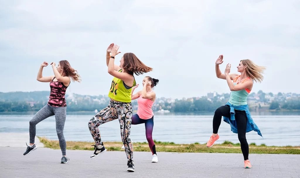 A group of young women in bright clothes, participating in an outdoor dance class.
