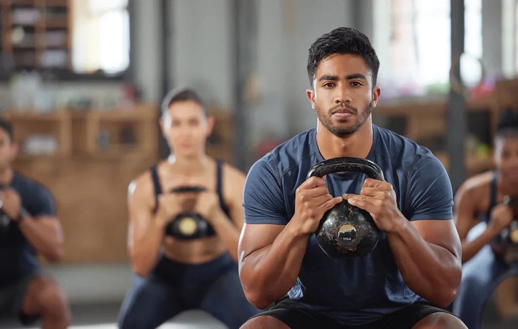 A man in a fitness studio performs an exercise with a kettlebell with the rest of the class behind him.