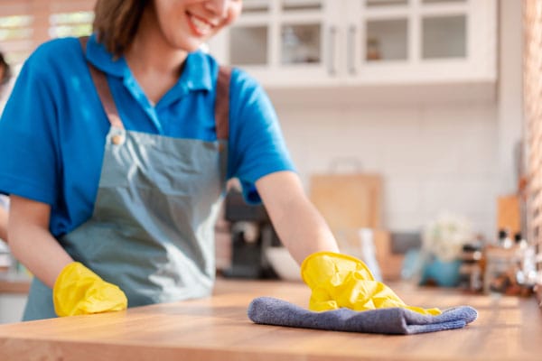 A woman wearing yellow rubber gloves wiping down a wood countertop