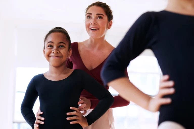 A dance teacher helps correct the pose of a young student.