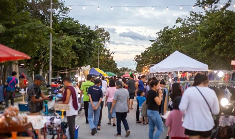 Outdoor street market at dusk with vendors lining a busy street full of patrons.