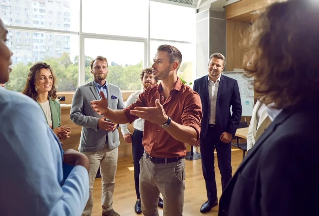 Life coach gestures while talking to a circle of businesspeople.