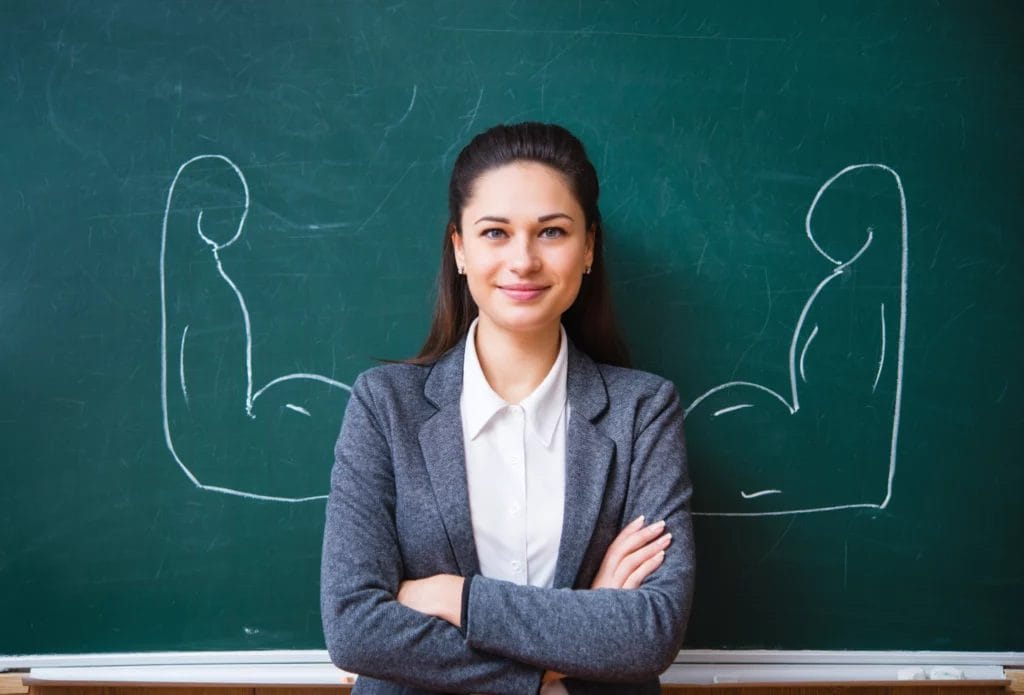 Confident teacher in front of illustrated arms flexing on a chalkboard