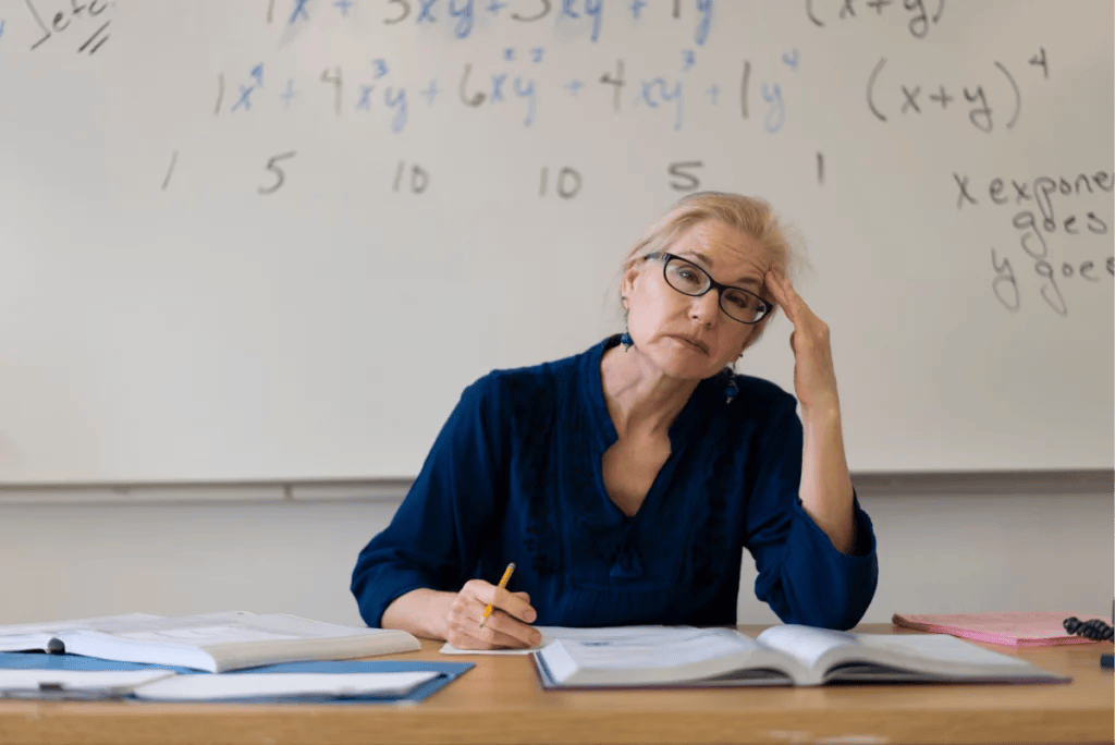 Tired math teacher at desk rubs her temple