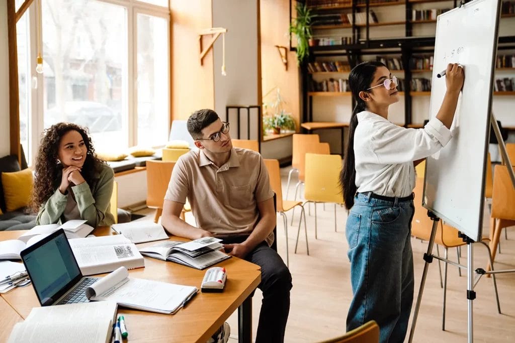 Students and a tutor at a whiteboard going over course material.