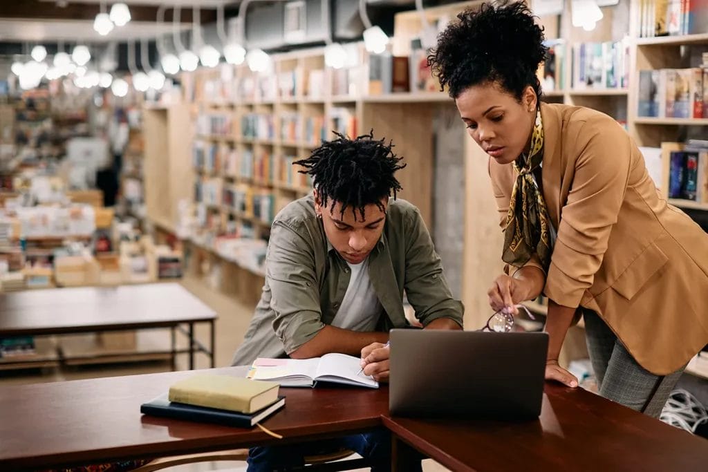 Student and tutor in library setting reading course material.