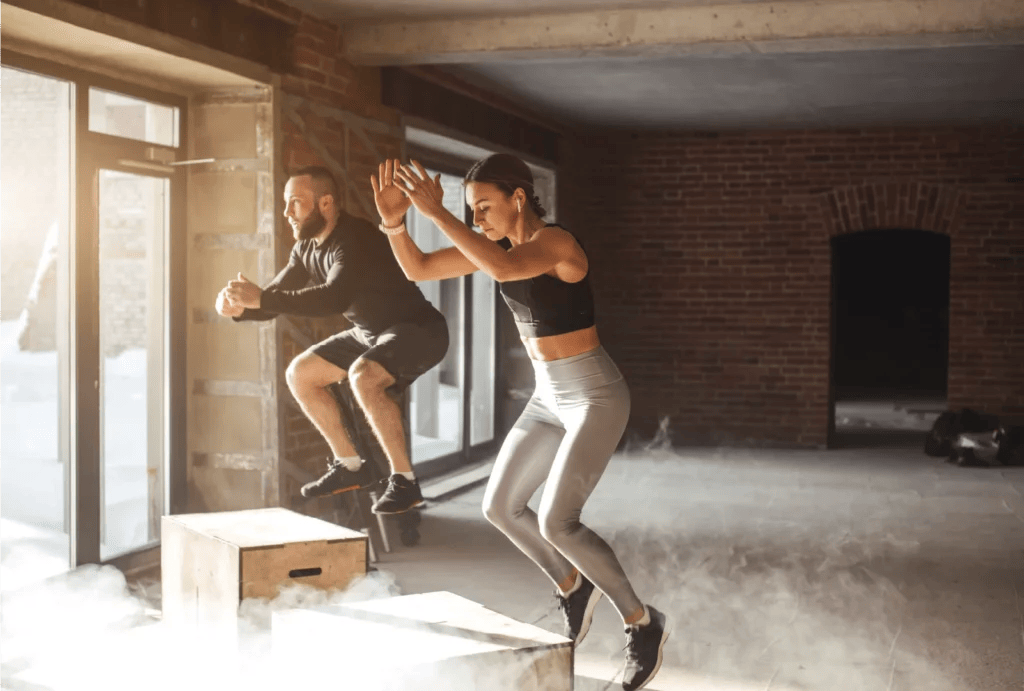 Two people doing box jumps in an empty crossfit gym