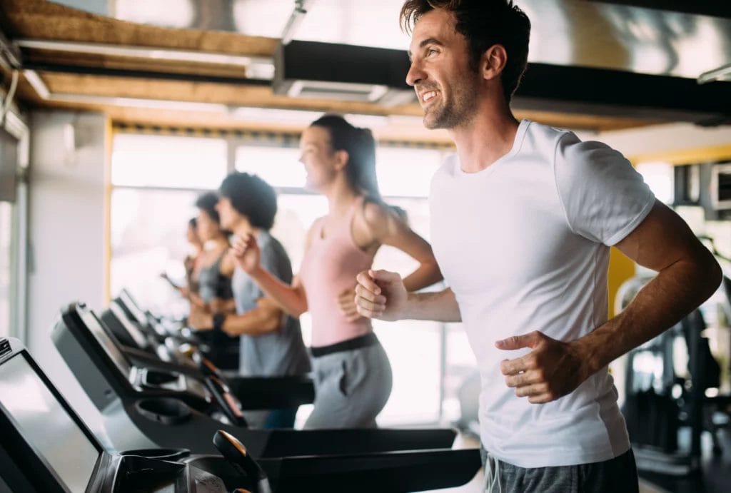 a row of gym goers running in a line on treadmills