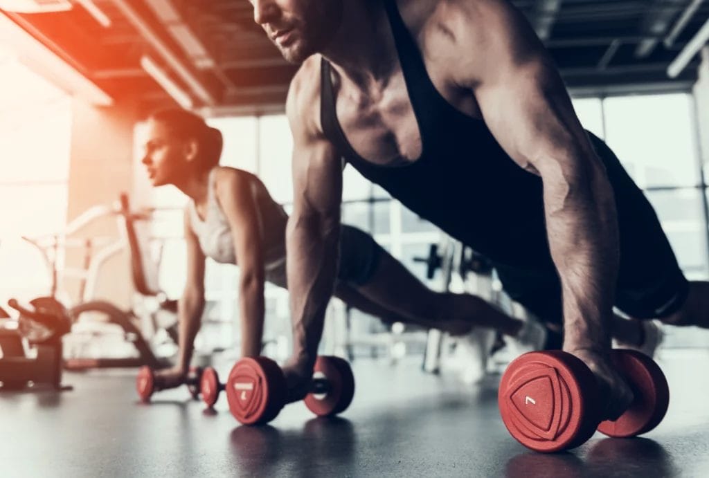 Two people do pushups while holding dumbells