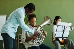 A music teacher helps his student play the baritone in a classroom.